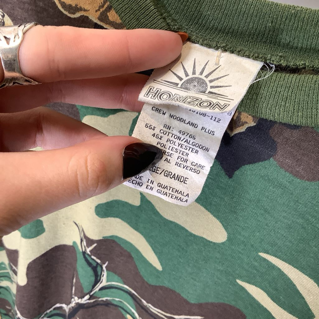 Hand holding a clothing tag on a camouflage-patterned fabric