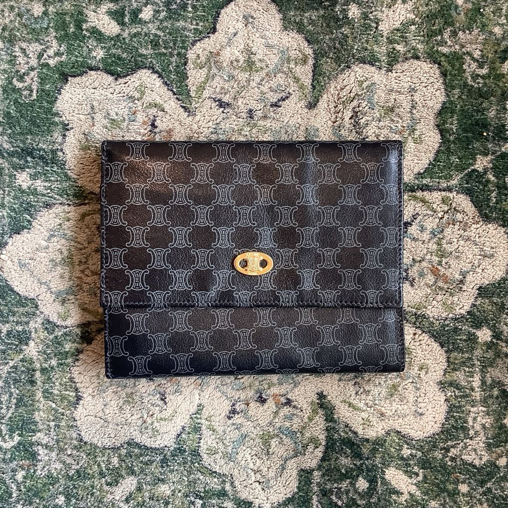 Black patterned wallet with gold emblem on a textured green surface