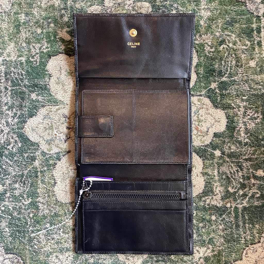 Open black leather wallet with visible brand logo on a textured green surface