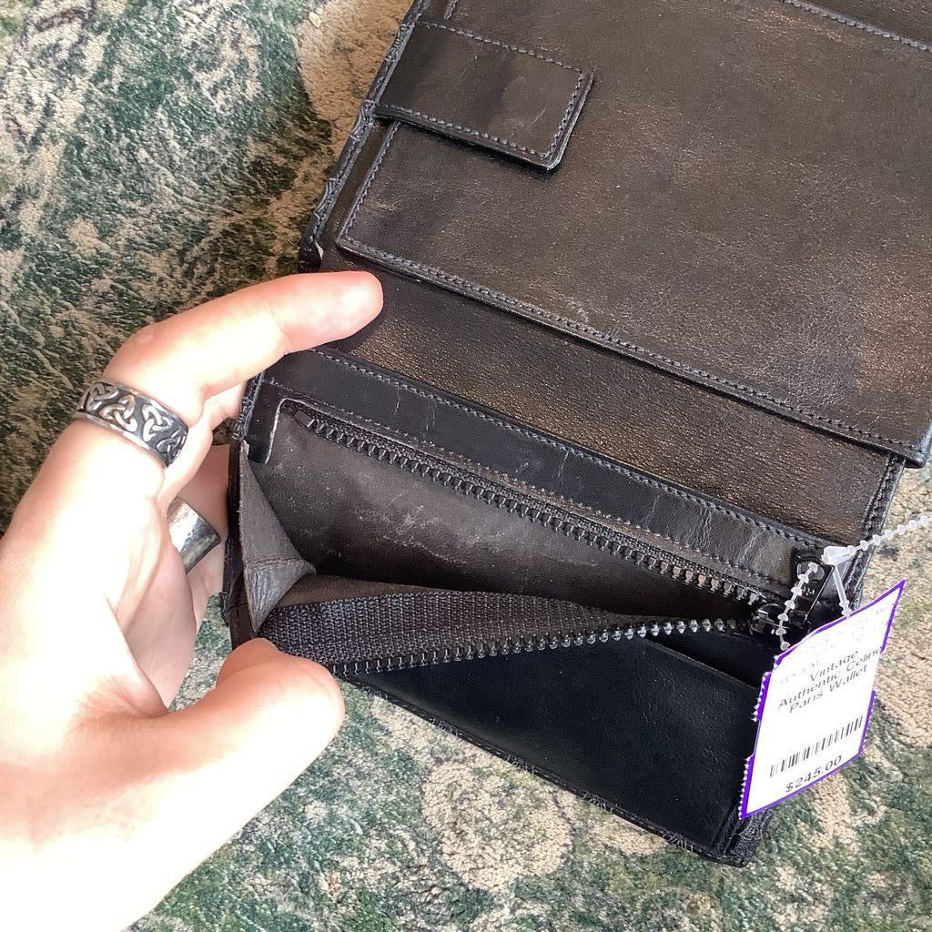 Black leather wallet with a visible brand tag held by a hand on a textured surface.