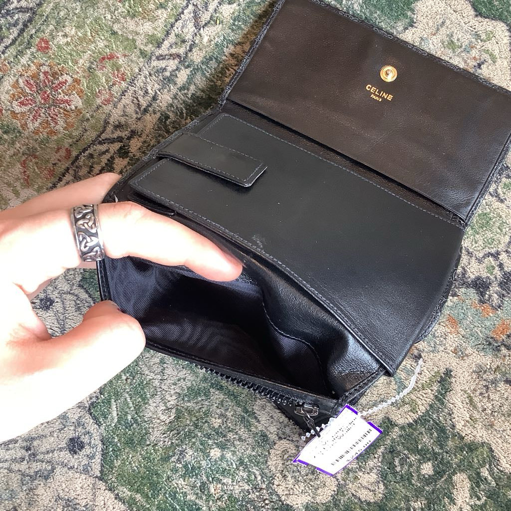 Black leather clutch bag with visible brand logo on a textured surface