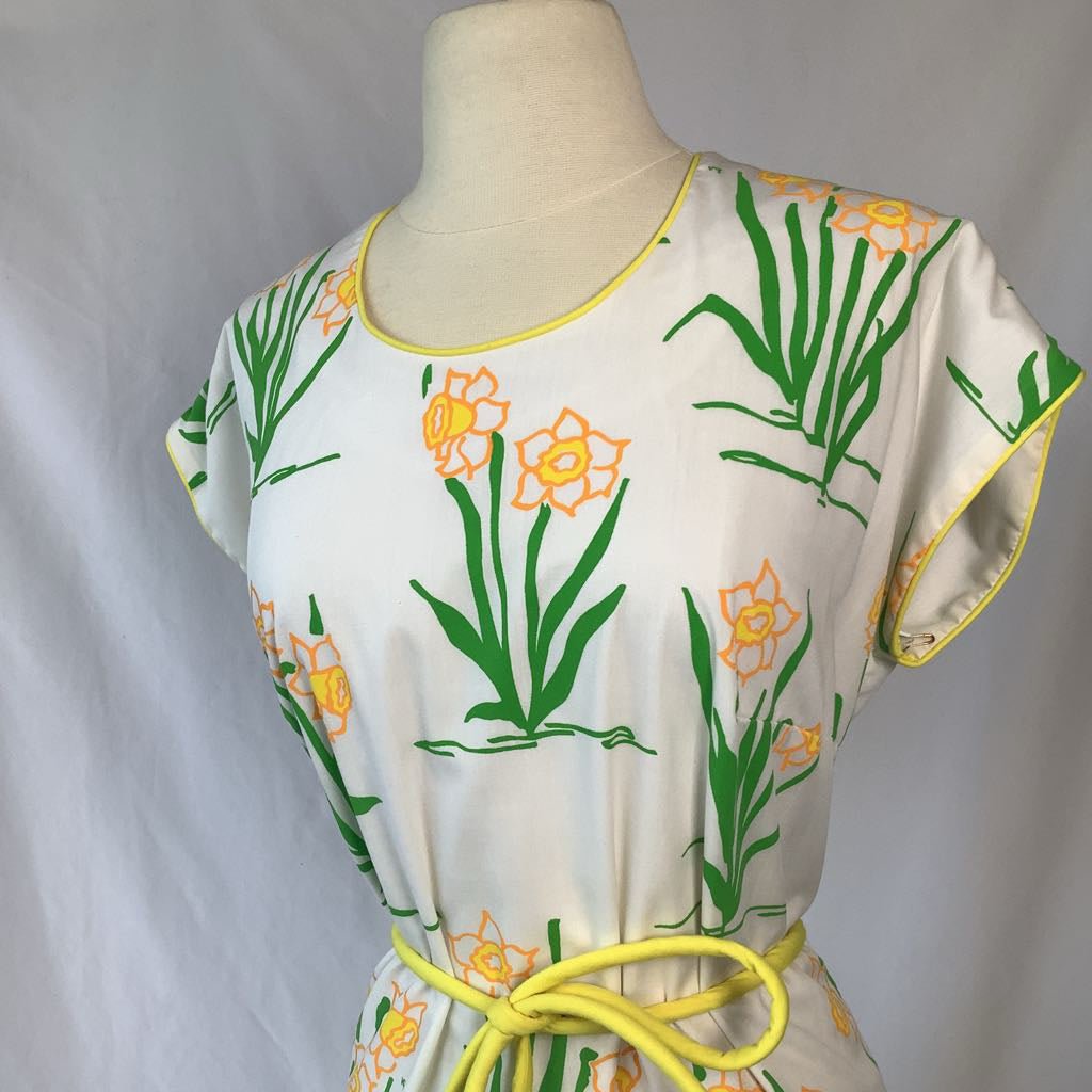 Mannequin wearing a white dress with green and orange floral patterns on a plain background