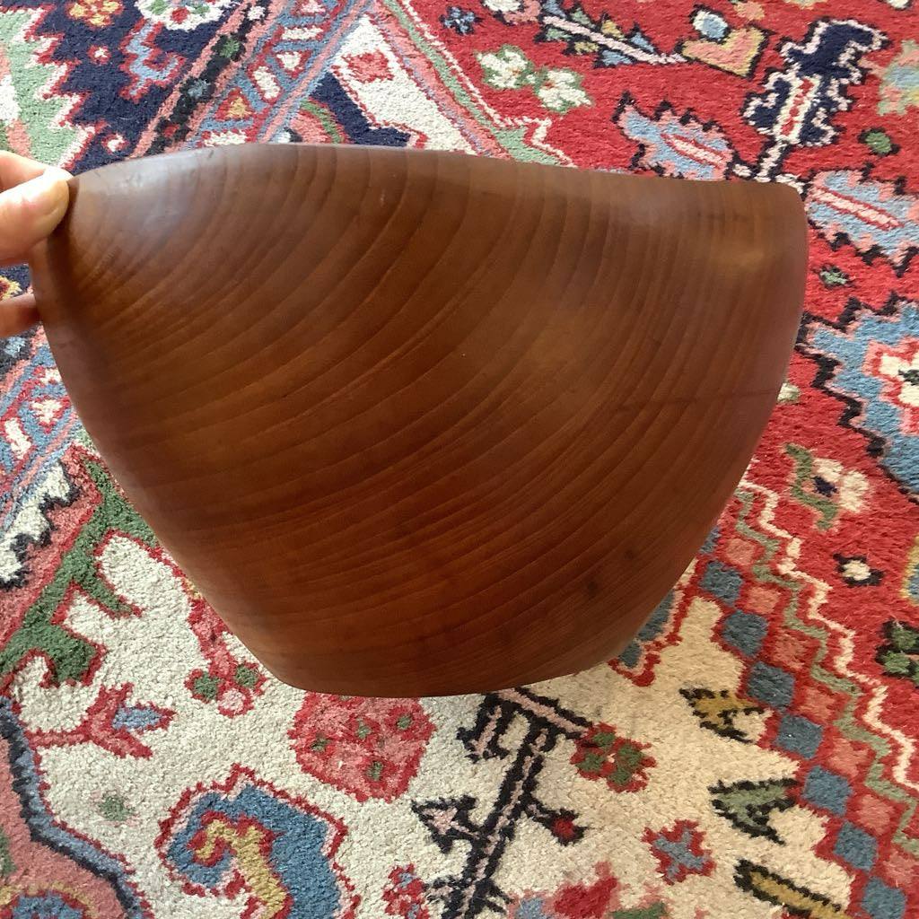 Wooden bowl held by a hand on a patterned rug