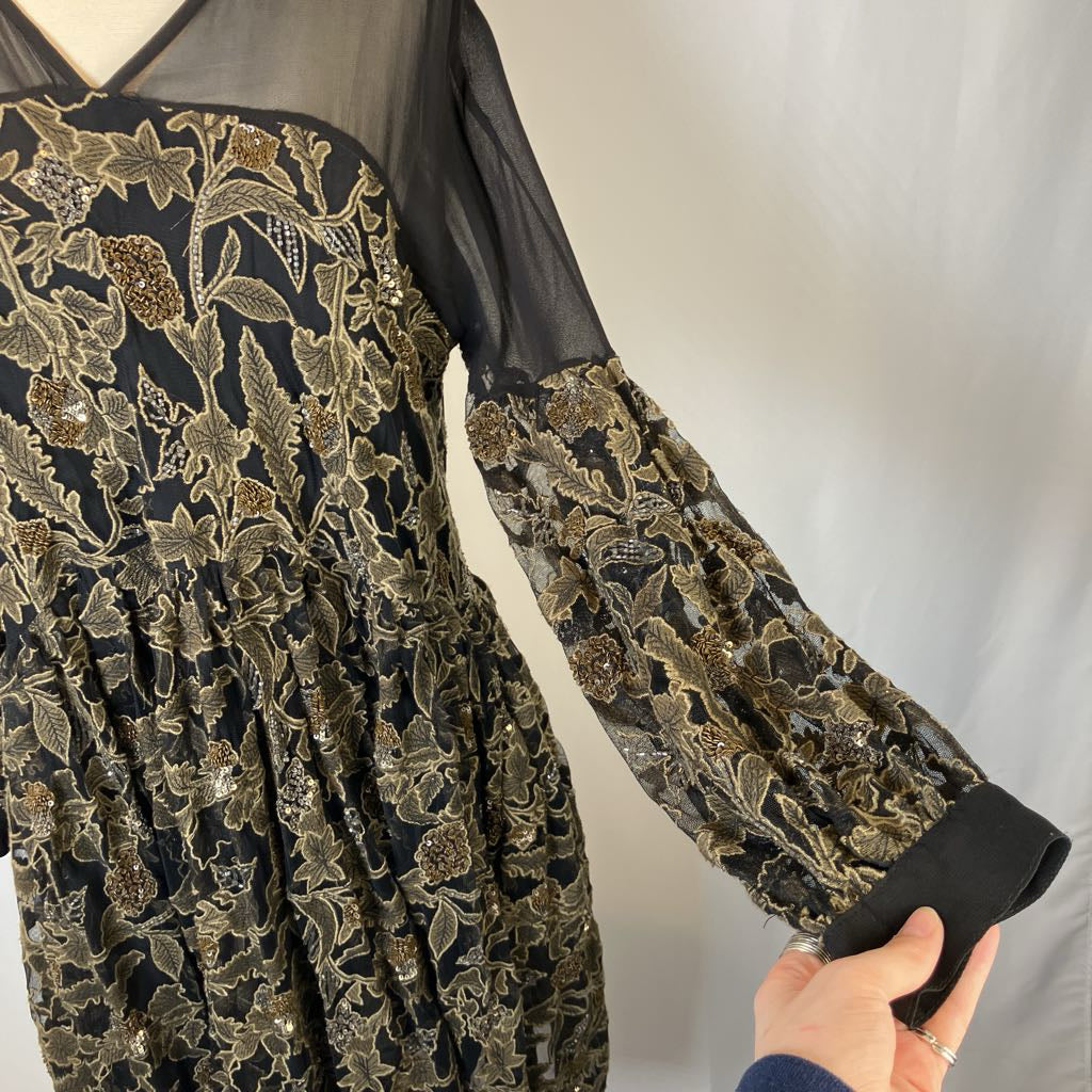 Black and gold embroidered garment with sheer sleeves on a white background