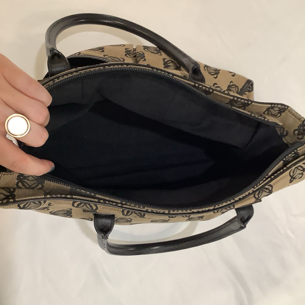 Handbag with a patterned exterior and plain interior, held open by a hand.