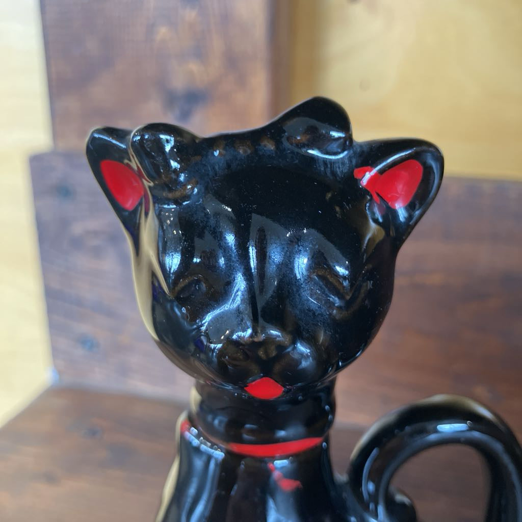 Black cat-shaped ceramic mug with red accents on a wooden surface.