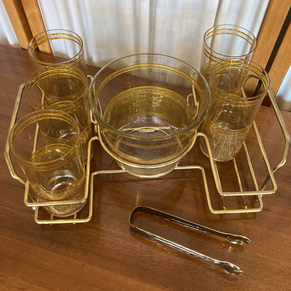 Overhead view of gold-detailed glasses on a metal tray with a pair of tongs in front of it all sitting on a wooden surface