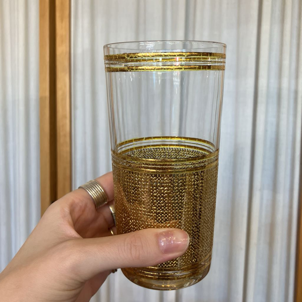 Hand holding a gold embossed glass up against a white fabric background