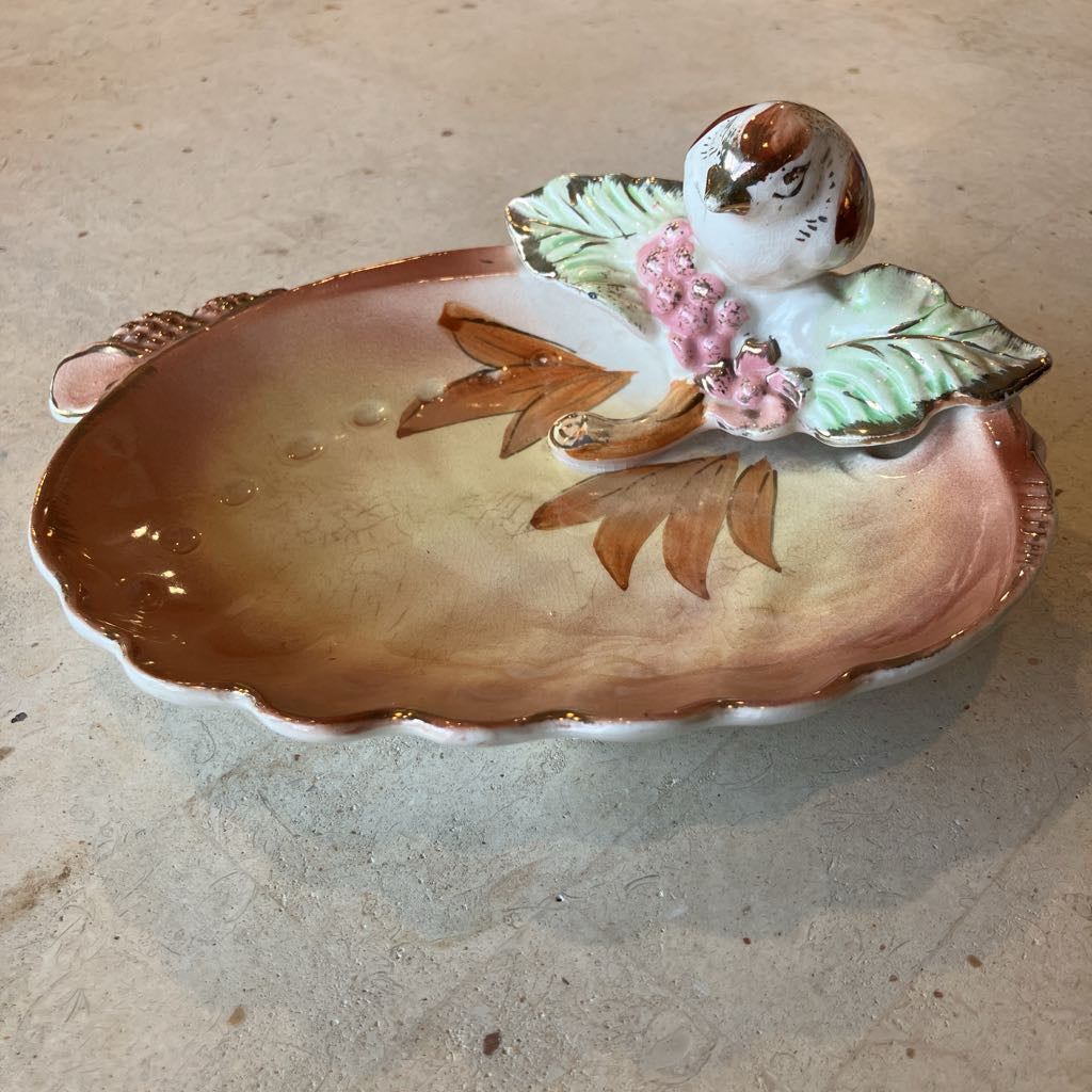Decorative ceramic dish with a bird and floral design on a shell shaped base