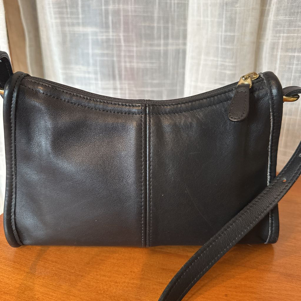 Black leather handbag on a wooden surface with a light curtain background