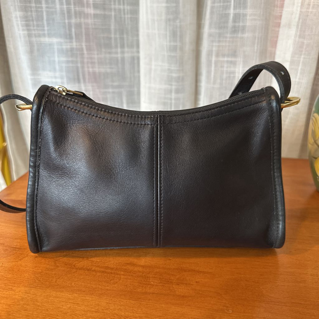 Black leather handbag on a wooden surface with a light curtain background