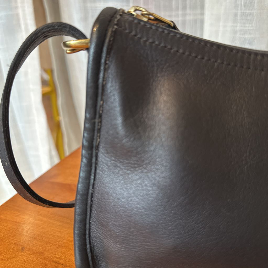 Close-up of a black leather handbag on a wooden surface with a blurred background