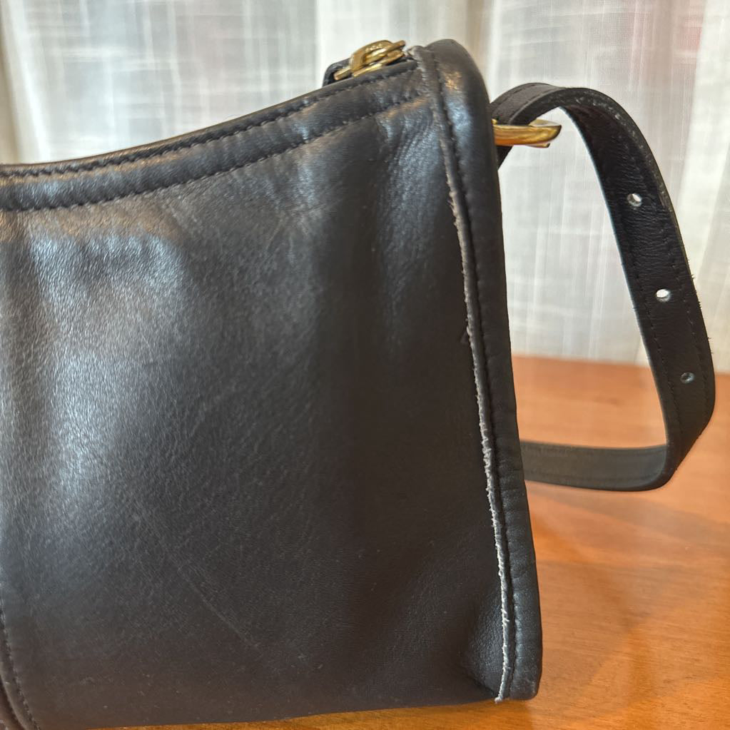 Black leather handbag on a wooden surface with a light curtain background