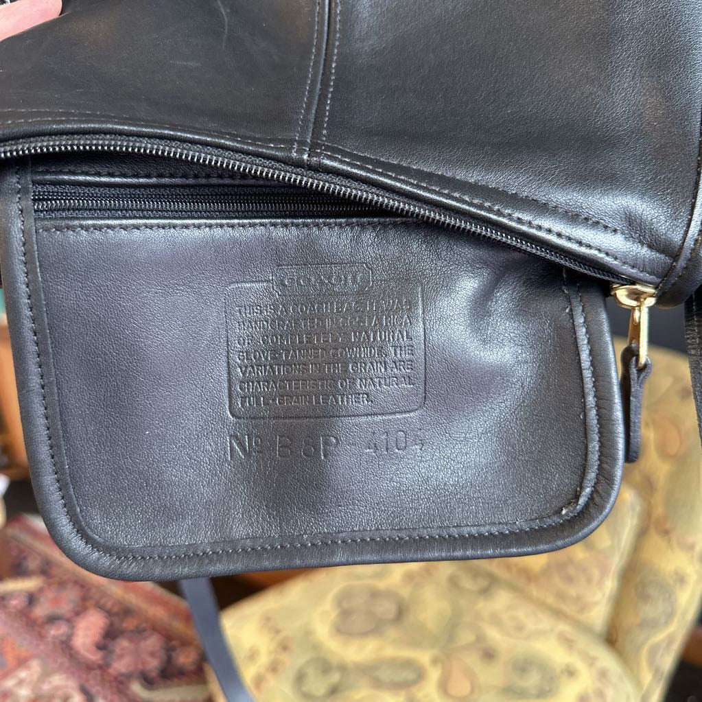Close-up of a black leather bag with a visible brand label on a patterned surface.
