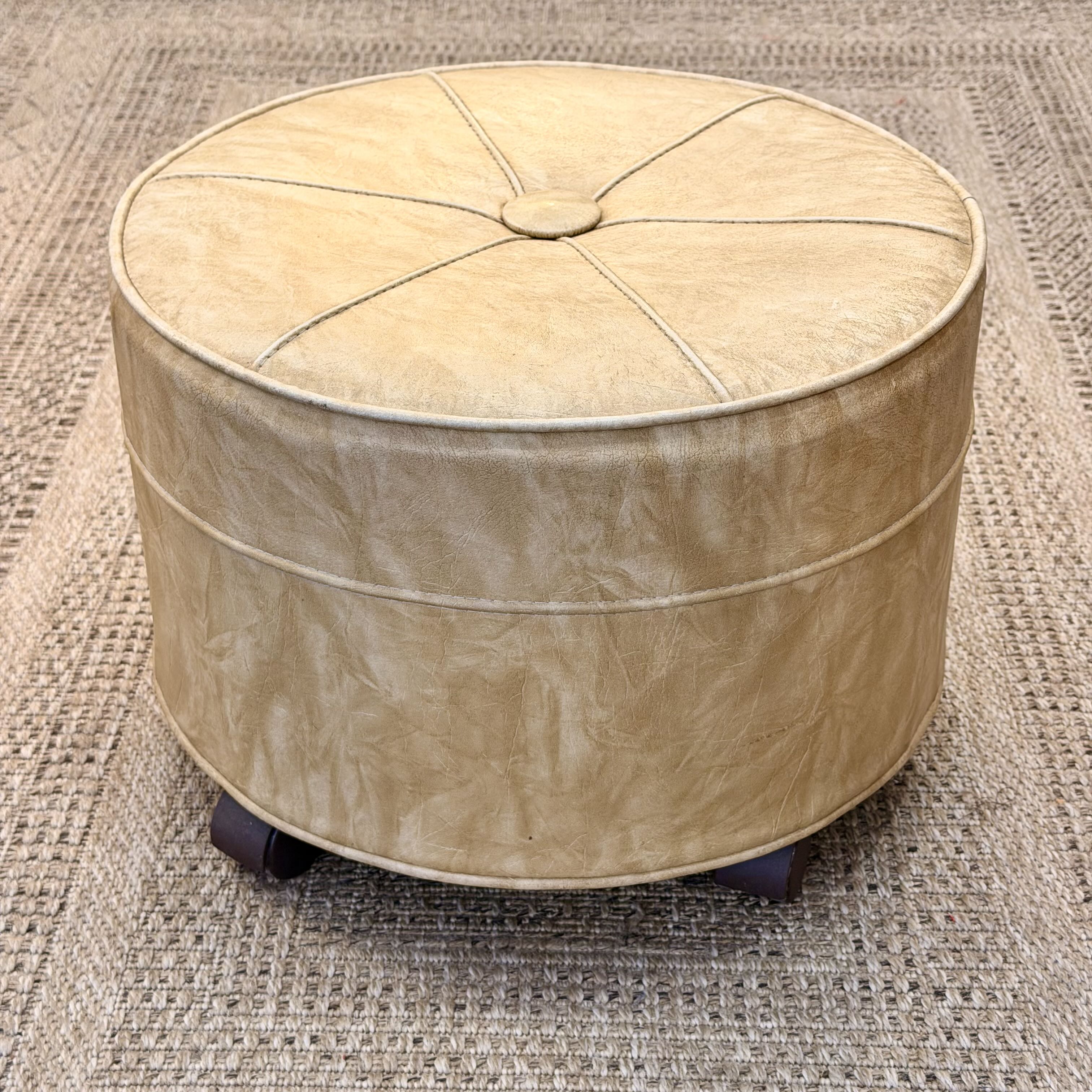 Round beige ottoman with a textured surface on a textured rug