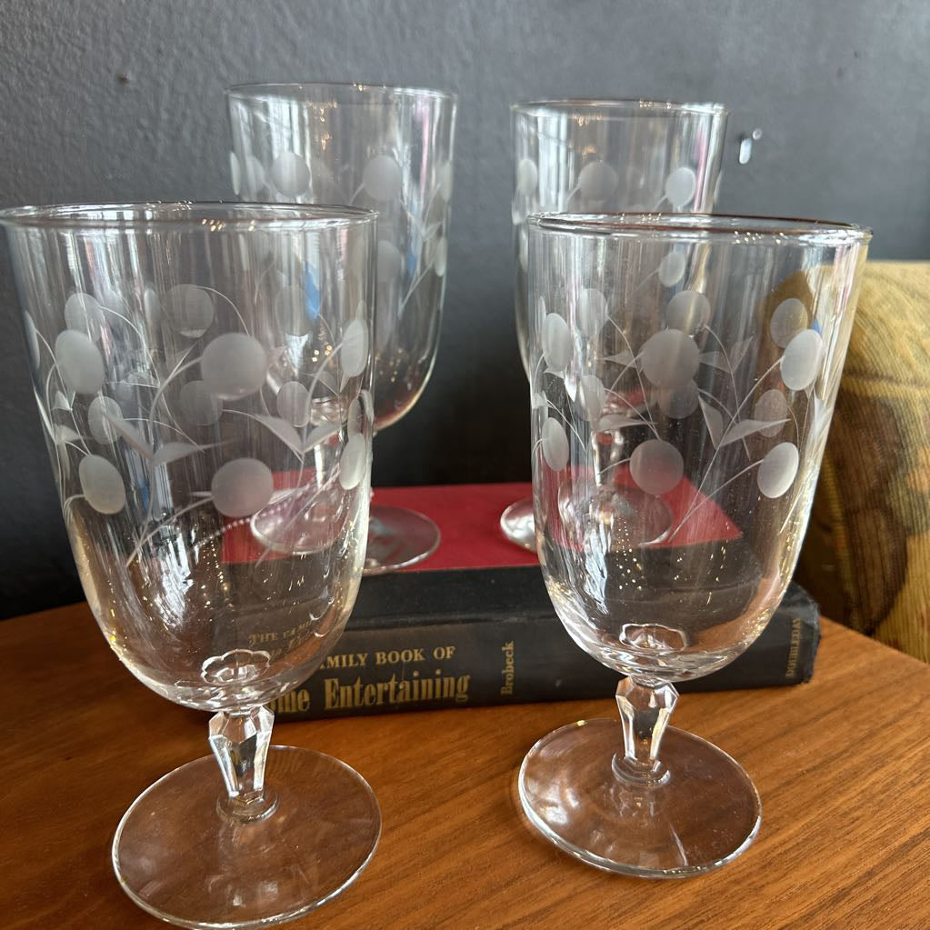 Four etched glass tumblers on a wooden surface with a book in the background.