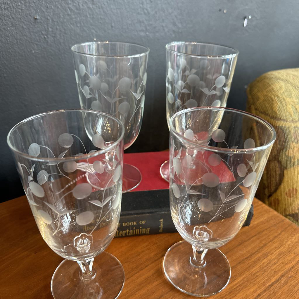 Four etched glass goblets on a wooden surface with a dark background