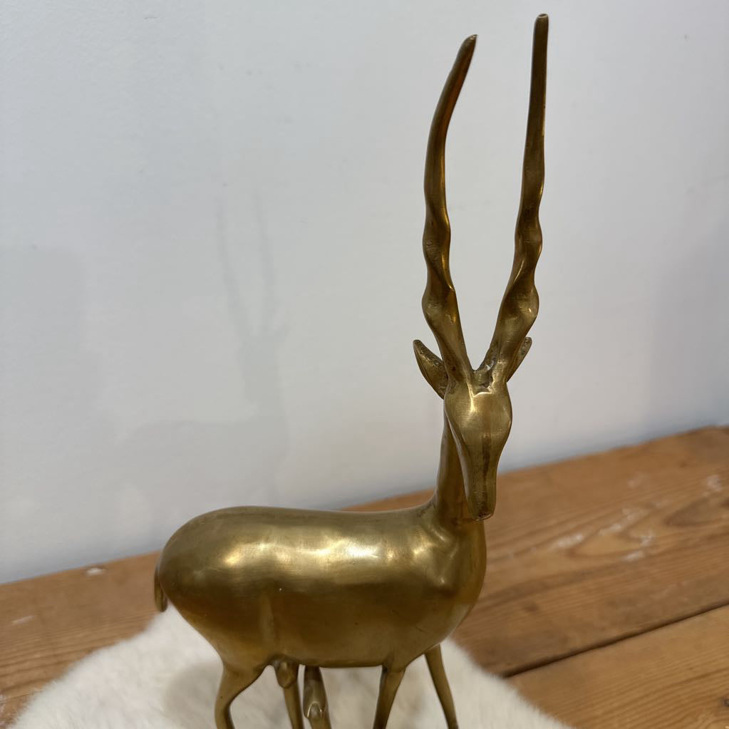 Brass deer figurine on a wooden surface with a white background