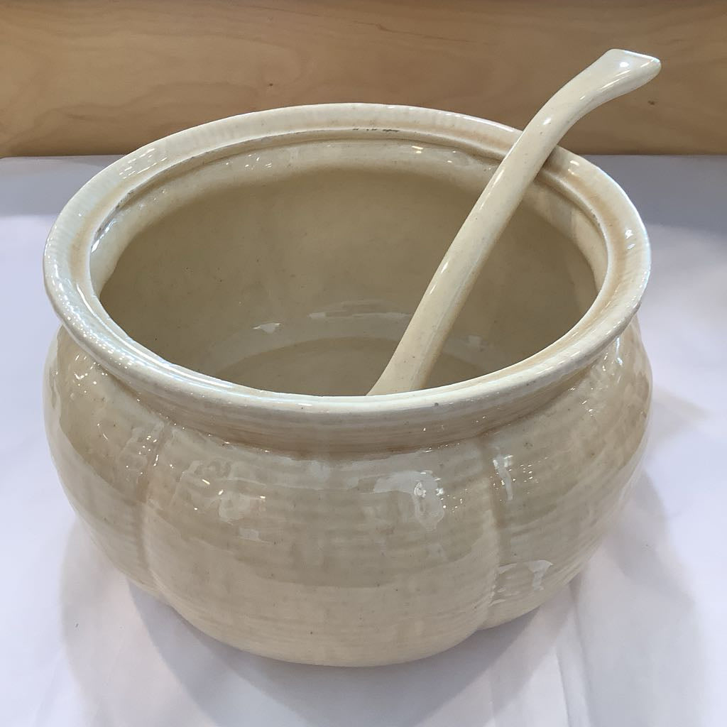 Beige ceramic jar with a spoon inside on a white surface.