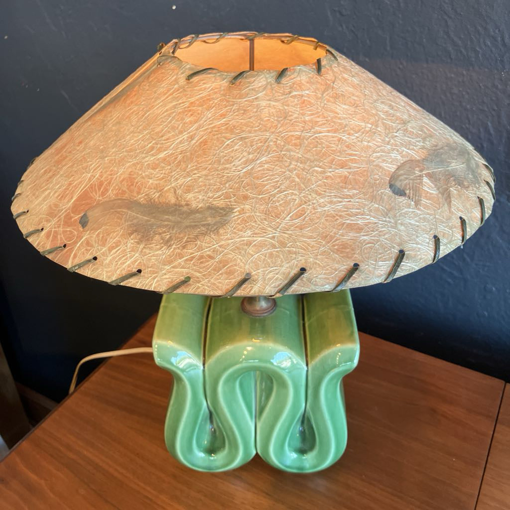 Green squiggly shape lamp base with brown fiberglass lamp shade on a wooden surface and with black background