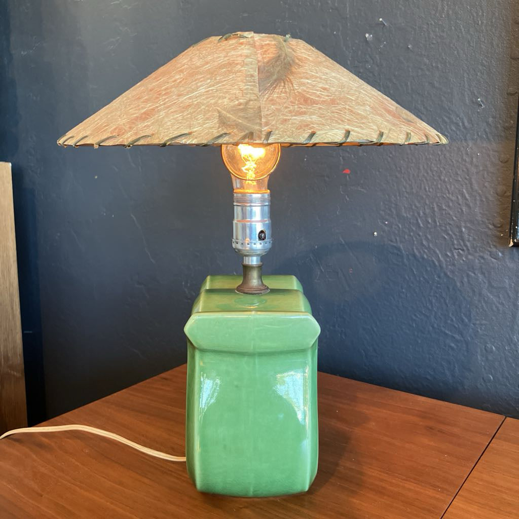 Green squiggly shape lamp base with brown fiberglass lamp shade on a wooden surface and with black background