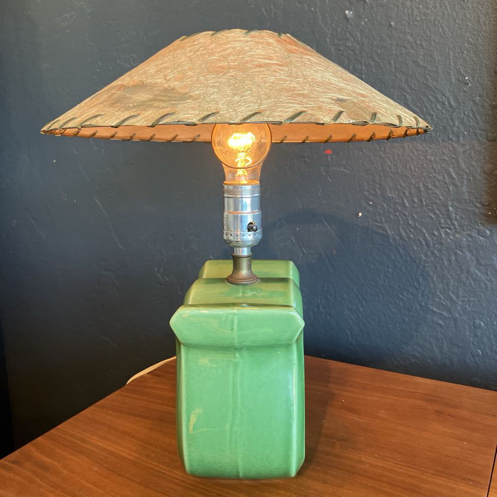 Green squiggly shape lamp base with brown fiberglass lamp shade on a wooden surface and with black background