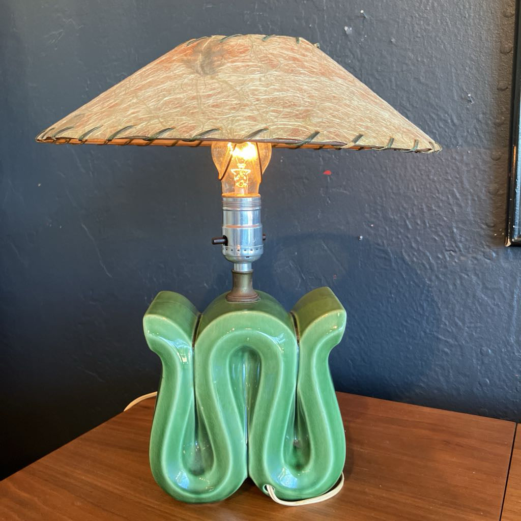 Green squiggly shape lamp base with brown fiberglass lamp shade on a wooden surface and with black background