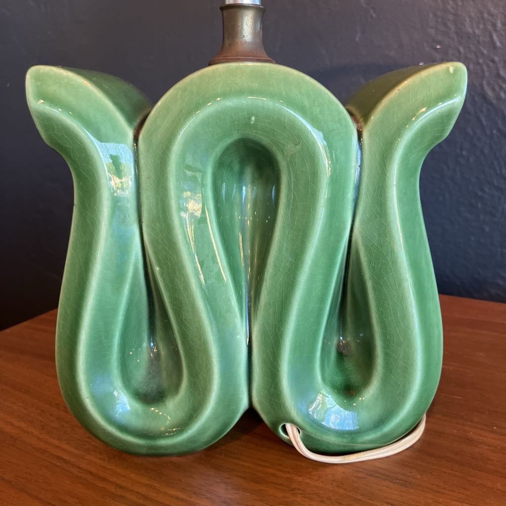 Green squiggly shape lamp base on a wooden surface and with black background