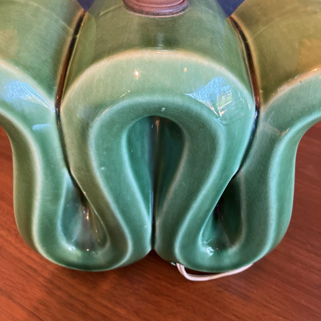 Green squiggly shape lamp base on a wooden surface and with black background