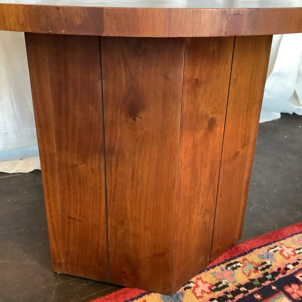 Wooden pedestal table with a textured surface on a dark floor.