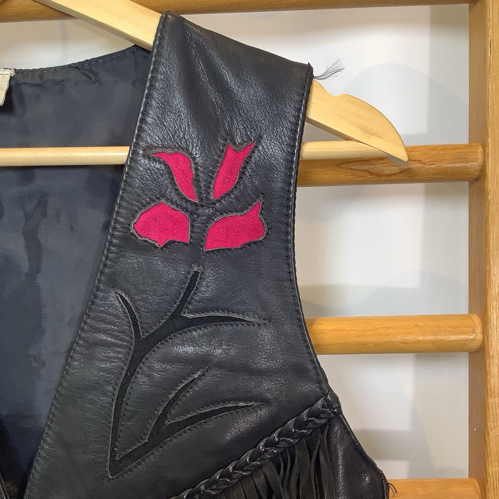 Black leather vest with pink floral design on a wooden rack