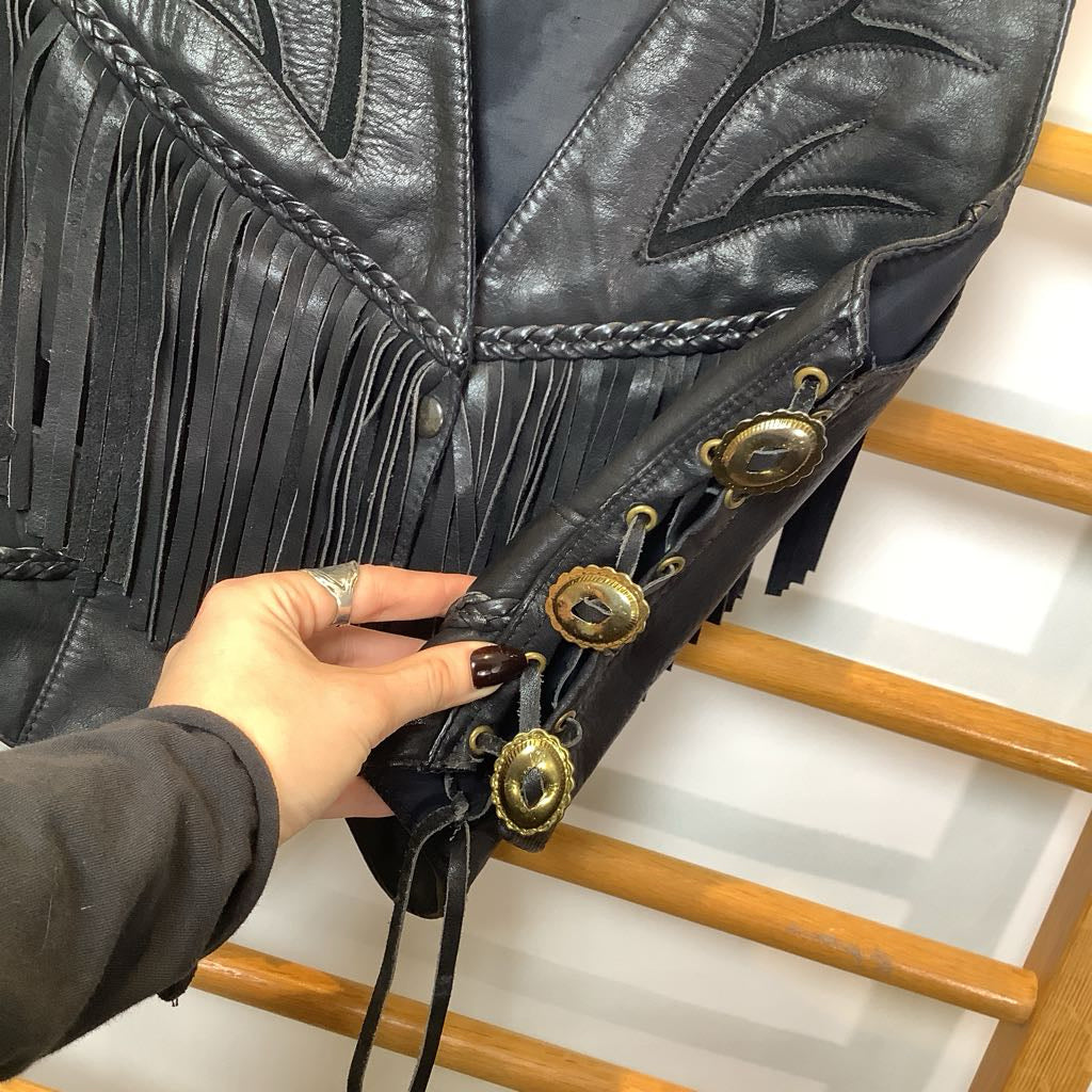 Close-up of a black leather boot with gold buttons and fringes, held by a hand.