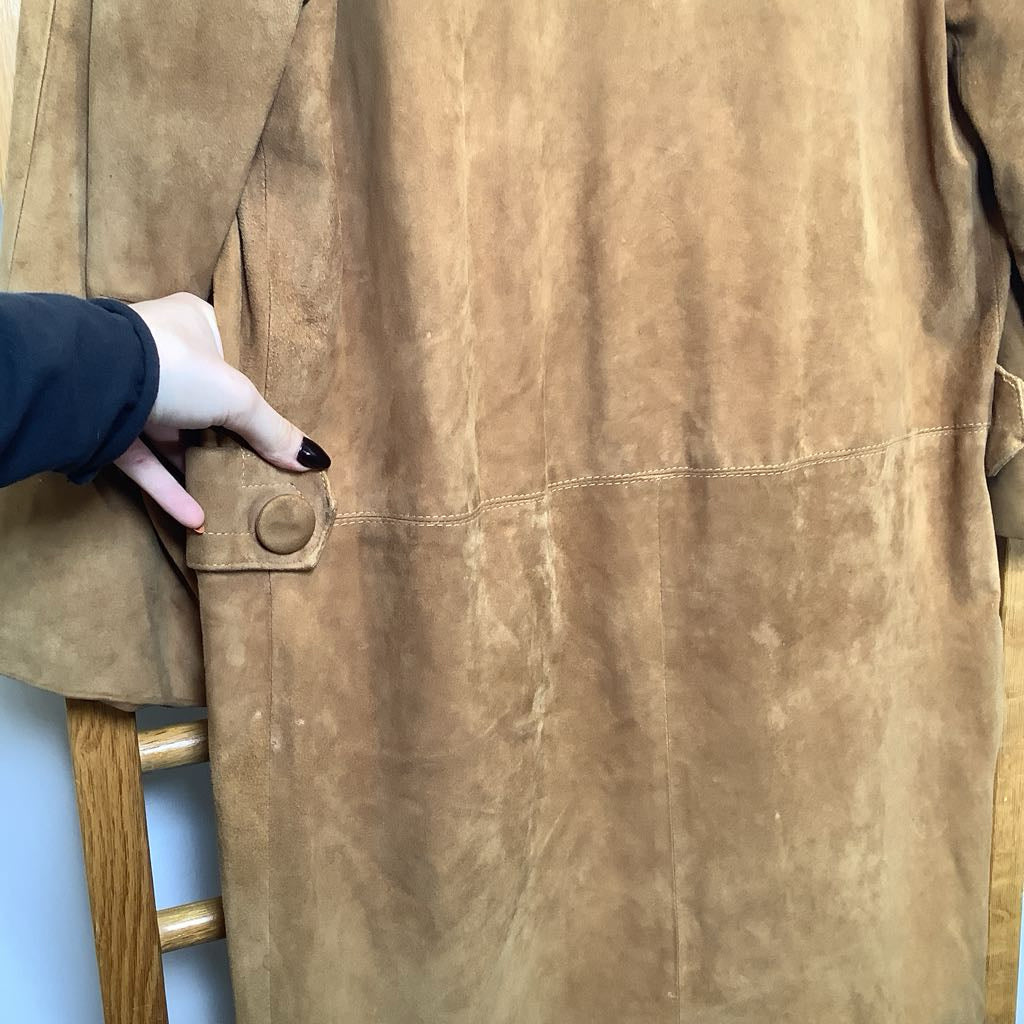 Close-up of a brown leather jacket with a hand touching a button, on a light blue background.