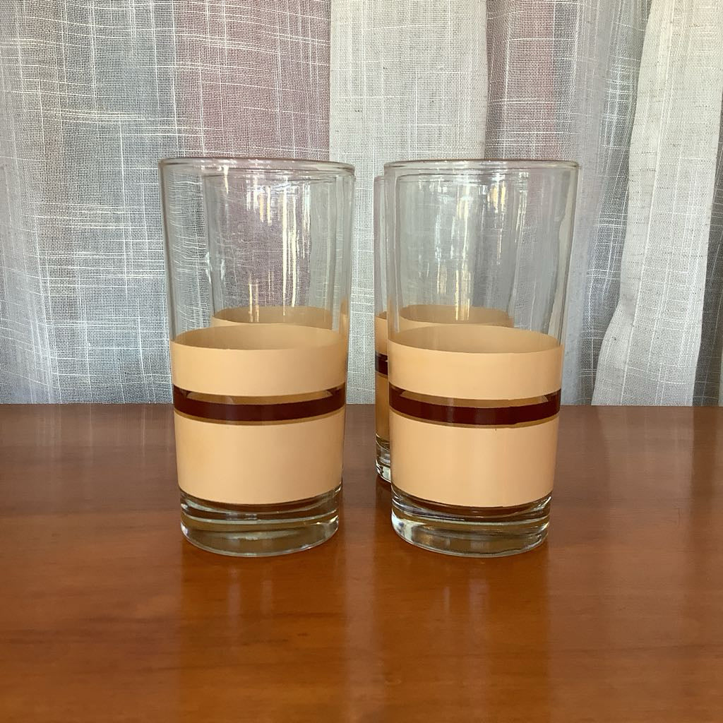 Two glass tumblers with beige bands on a wooden surface and curtain background