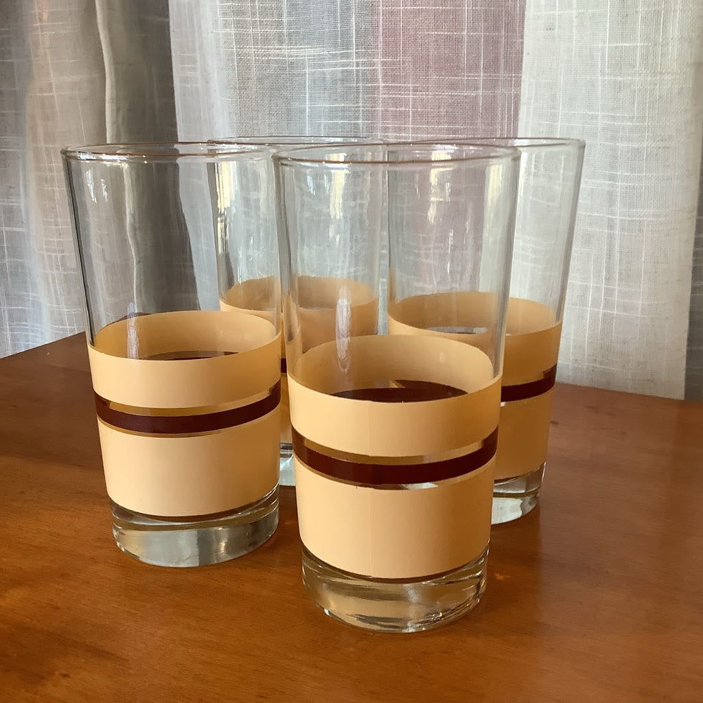 Four glass tumblers with beige bands on a wooden surface