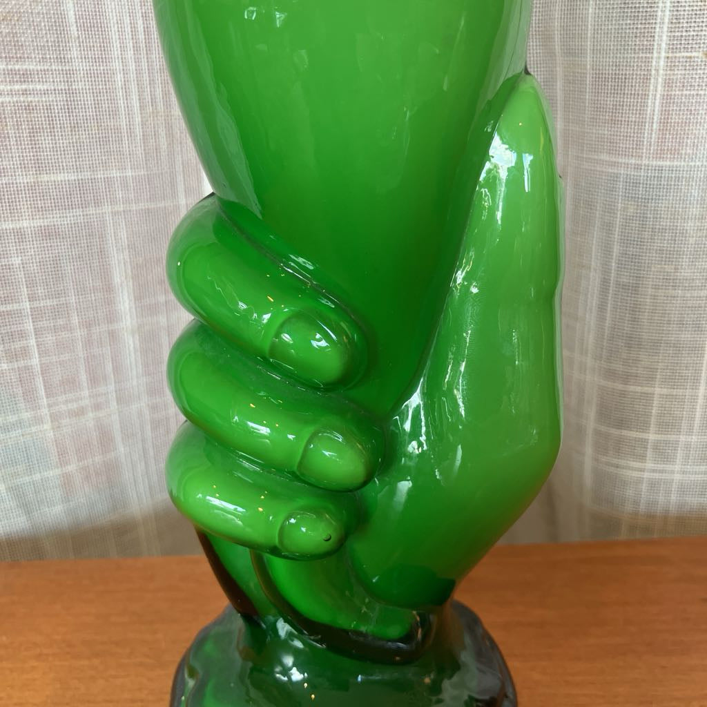 Green glass sculpture of a hand on a wooden surface with a neutral background