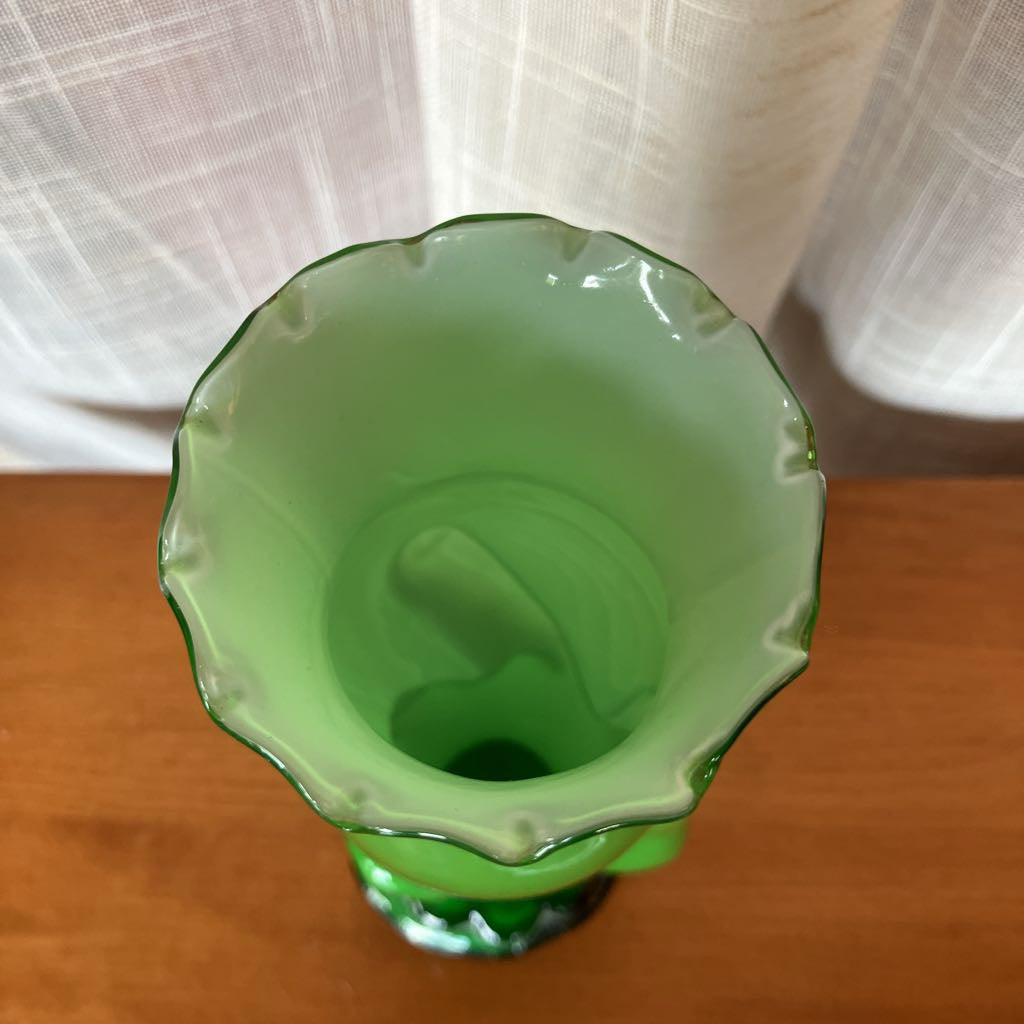 Green glass vase shaped like a hand holding a vase against a textured white curtain background.