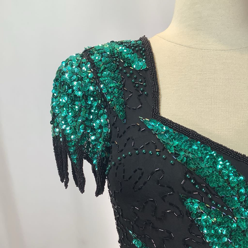 Black dress with green beading on a mannequin against a neutral background