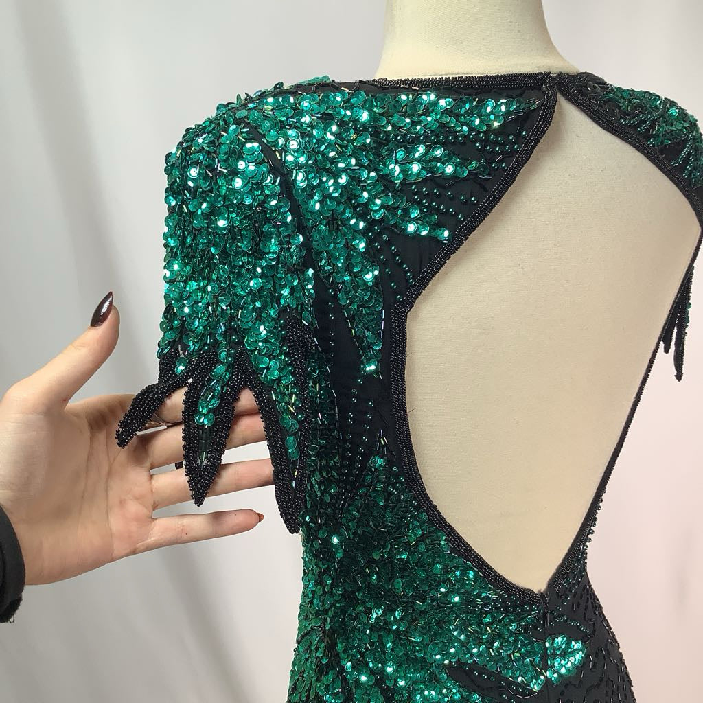 Green and black beaded dress on a mannequin with a hand for scale.