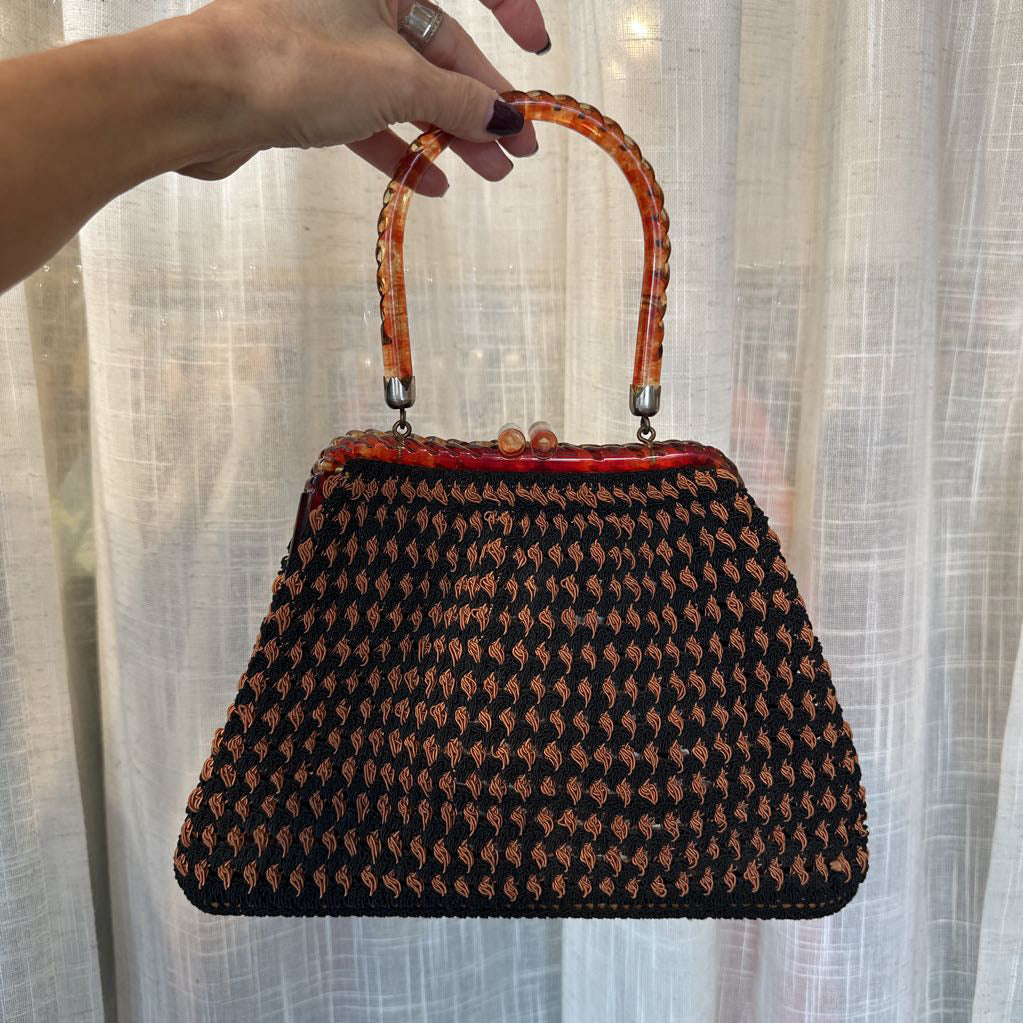 Handbag with patterned design held by a hand against a light curtain background