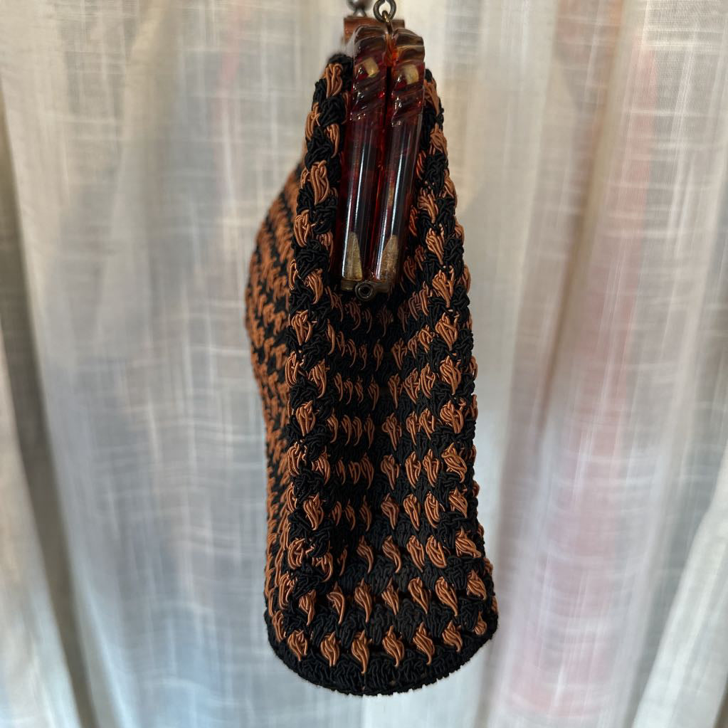 Black and brown woven pouch with a decorative bead on a sheer white curtain background