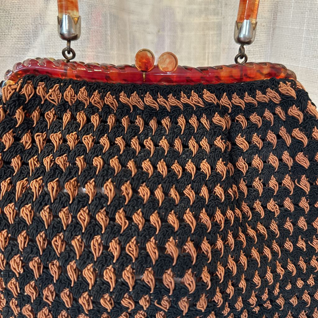 Vintage handbag with black and orange patterned body and red handle.