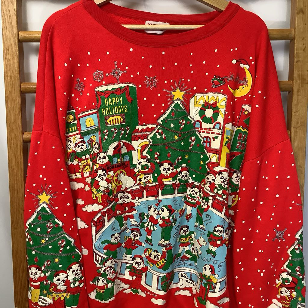 Red Christmas-themed sweatshirt with festive designs on a wooden rack.