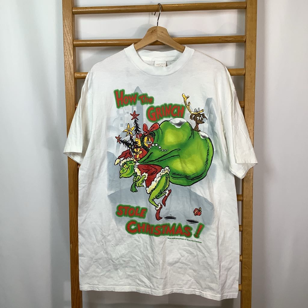 White t-shirt with 'How the Grinch Stole Christmas!' graphic on a wooden rack.