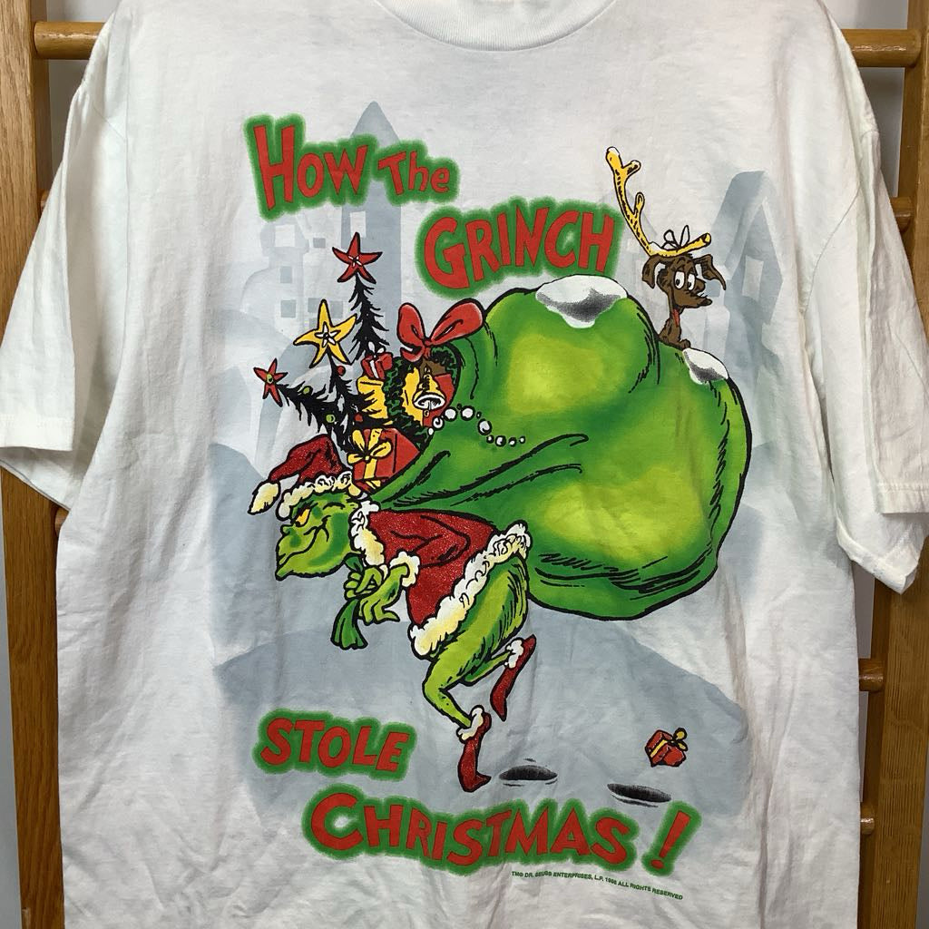 White t-shirt with 'How the Grinch Stole Christmas!' graphic design on a wooden rack.