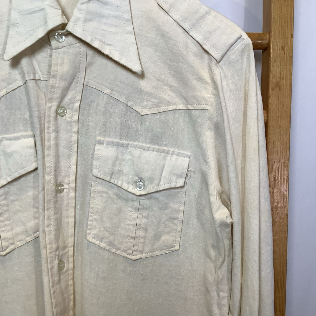 Light-colored shirt with a pocket on a wooden hanger against a white wall