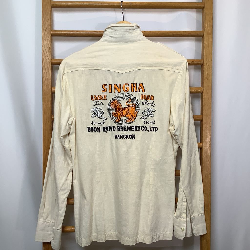 Beige shirt with Singha Beer branding on a wooden rack against a white background