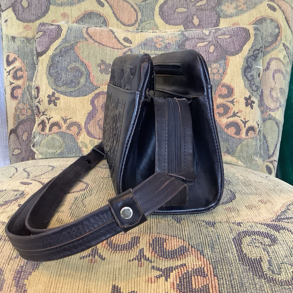 Black leather bag with strap on a patterned chair