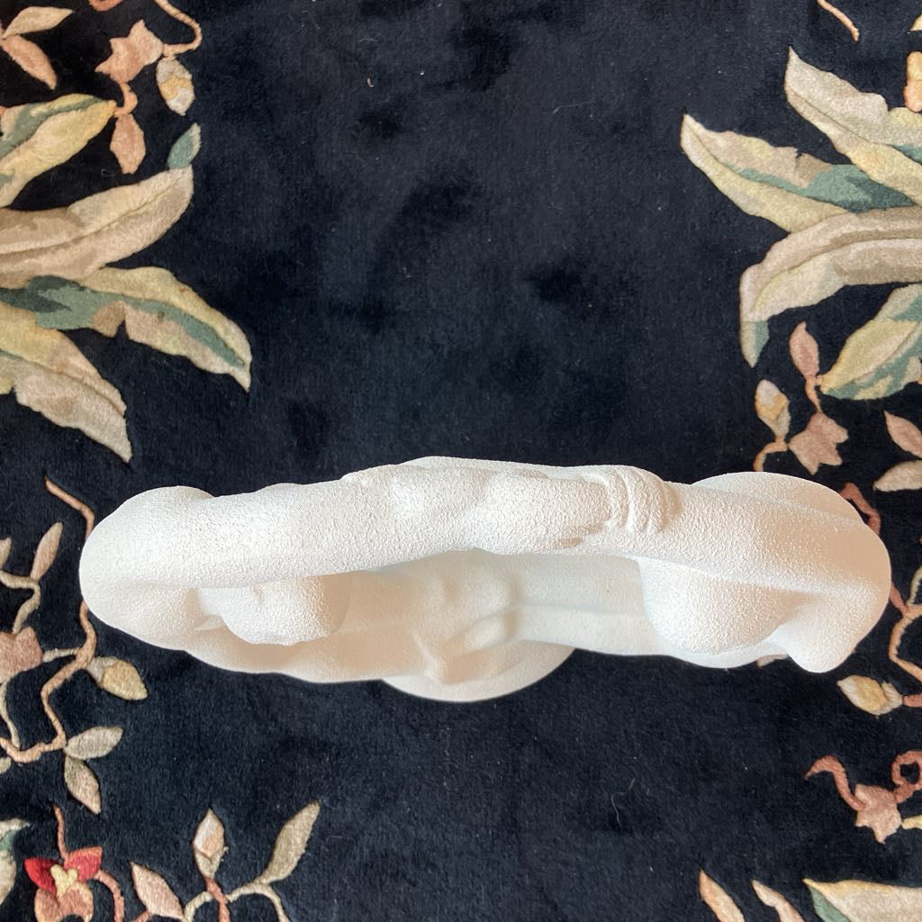 White ceramic sculpture on a dark floral-patterned fabric background