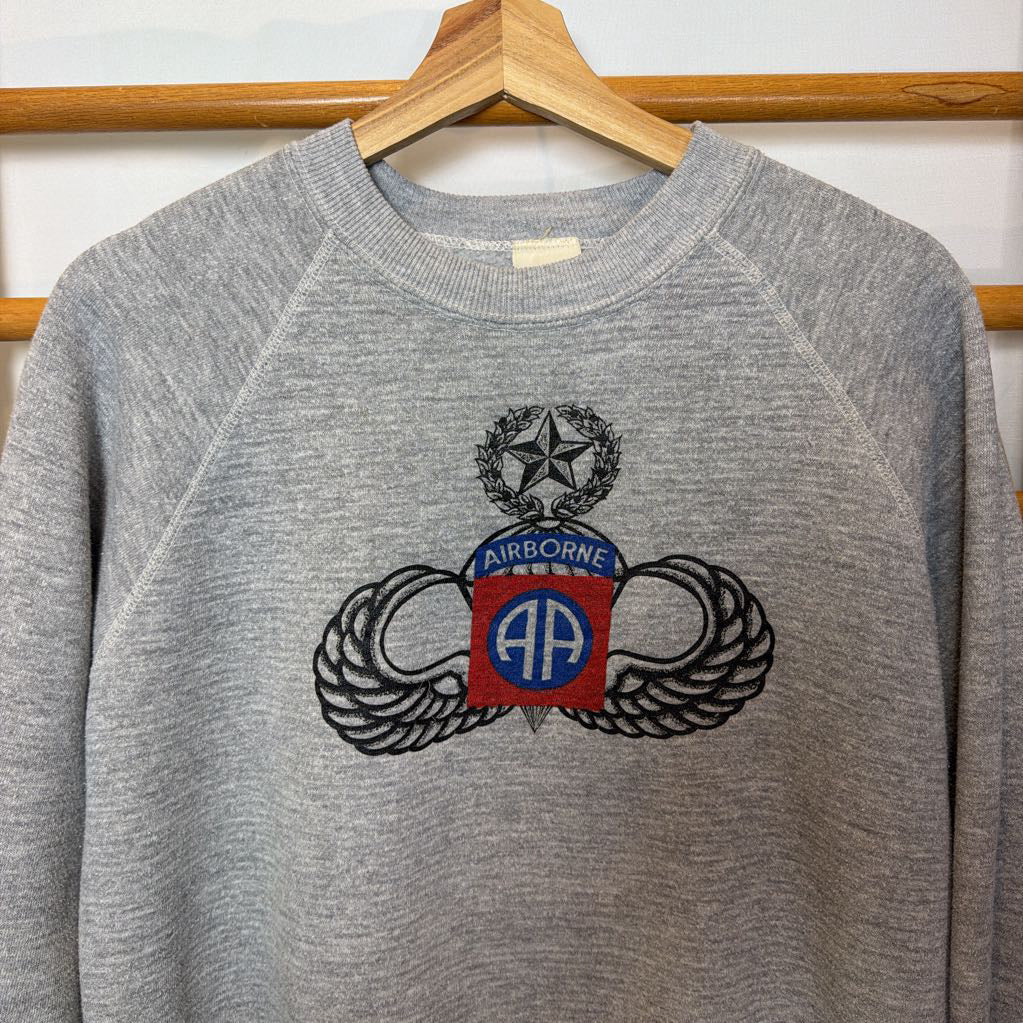 A gray sweatshirt that has a logo and the word "Airborne" on the front hanging on a wooden rack.